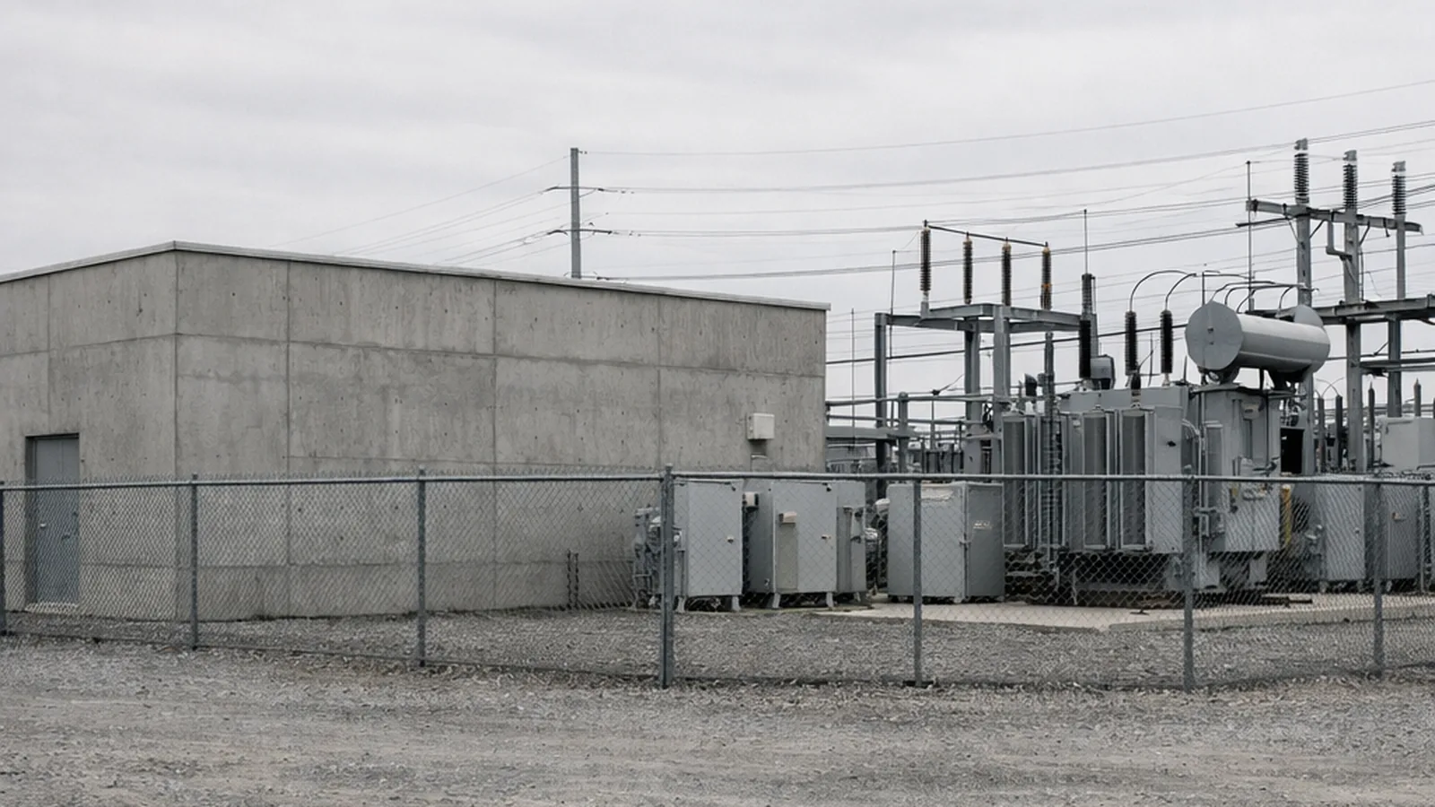A plain concrete utility building with transformers and switchgear behind a fence.