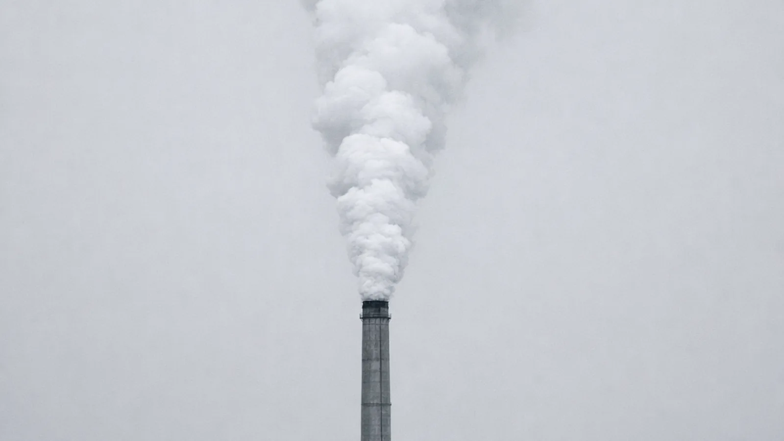 Steam venting from an industrial stack straight up into an empty winter sky, nothing capturing it.